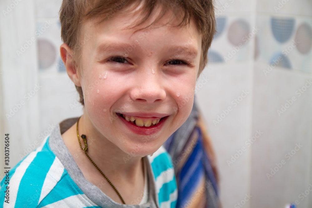 A teenage boy washed his face with cold water. Drops of water on the baby's cheeks and nose. The baby smiles and rejoices. Morning.
