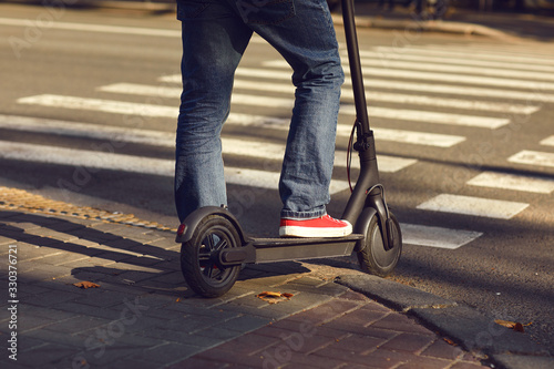 Fotografia Legs of a man in jeans and sneakers on an electric scooter at a crosswalk on a c