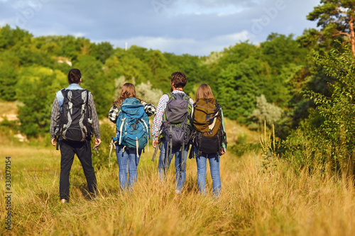 Young people with backpacks stand in the forest from behind.