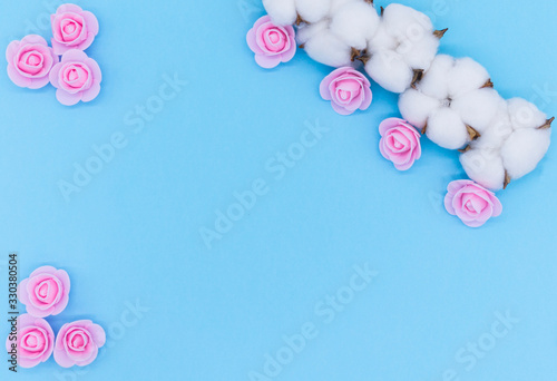 A branch of cotton and pink roses on blue background. Copyspace for your text. Flatlay, top view. Romantic concept.