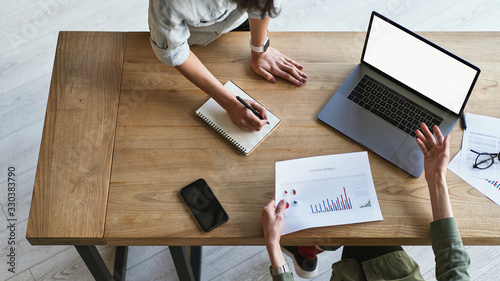 Top view of two businesswoman analysing, making notes on graphics and charts