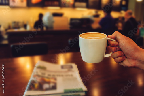 Fototapeta Male hands holding cup of coffee on table in cafe