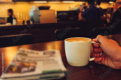 Fototapeta Male hands holding cup of coffee on table in cafe