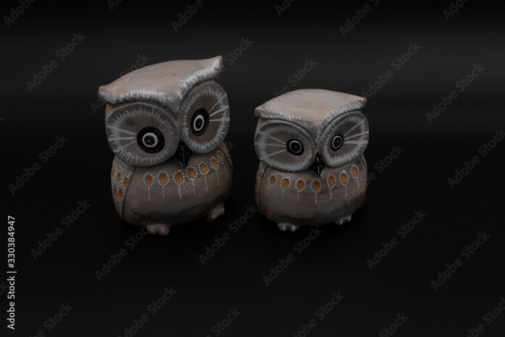 Naklejka premium Figure of a pair of wooden owls one bigger than another on black background