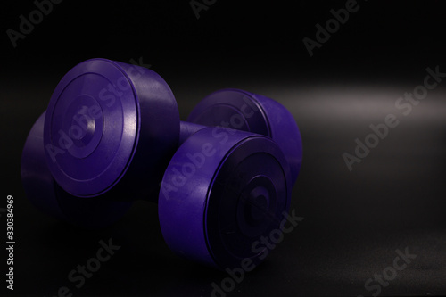 Two purple dumbbells one on another with dark background. Wellness concept