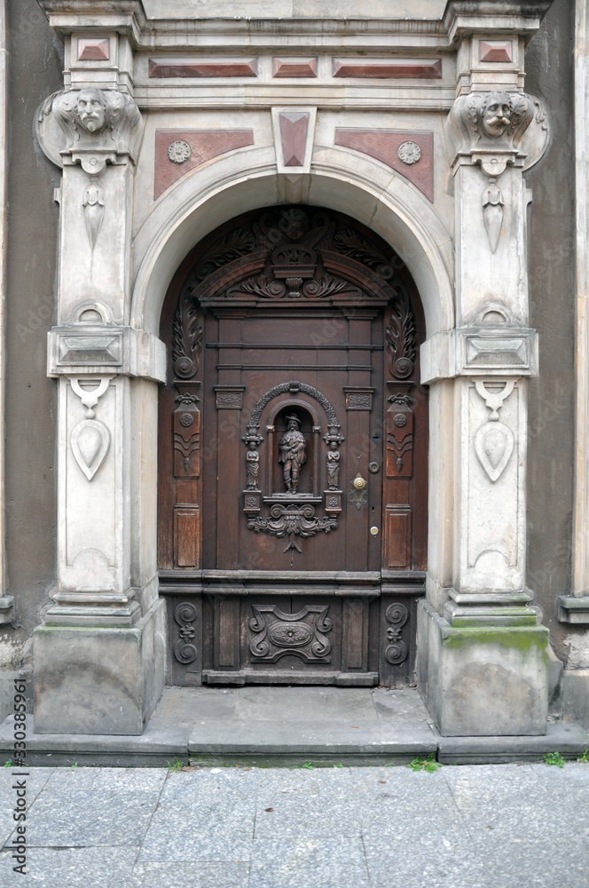 An old carved wooden door, with elements of forging, framed by sculptures. The facade is in the Baroque style. Poland, Gdansk 2019.