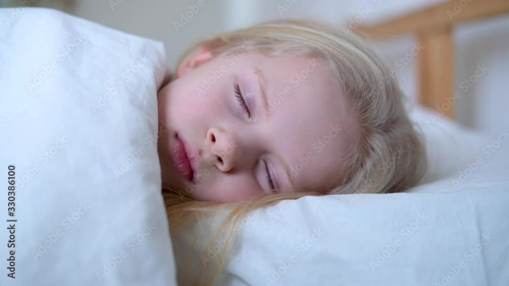 Sleeping little blonde girl close up in big bed with white bedding early in the morning. Children dream. Childhood, calm, night .4k footage Sleeping little blonde girl close up in big bed with white bedding early in the morning. Children dream. Childhood, calm, night .4k footage
