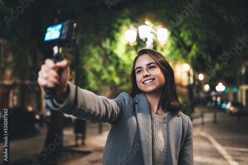 Female vlogger record with digital camera. Smiling woman taking selfie video on light night city. Traveler making video for her blog. Vlogger uses photo camera for shoot social media photo
