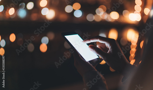 person texting text message on background blur color light night city, hipster touch on template screen mobile phone, girls holding in hands smartphone, mockup blank screen