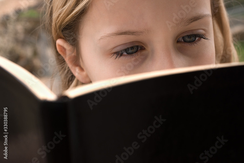  Cute schoolgirl reading the book in the open air, close up