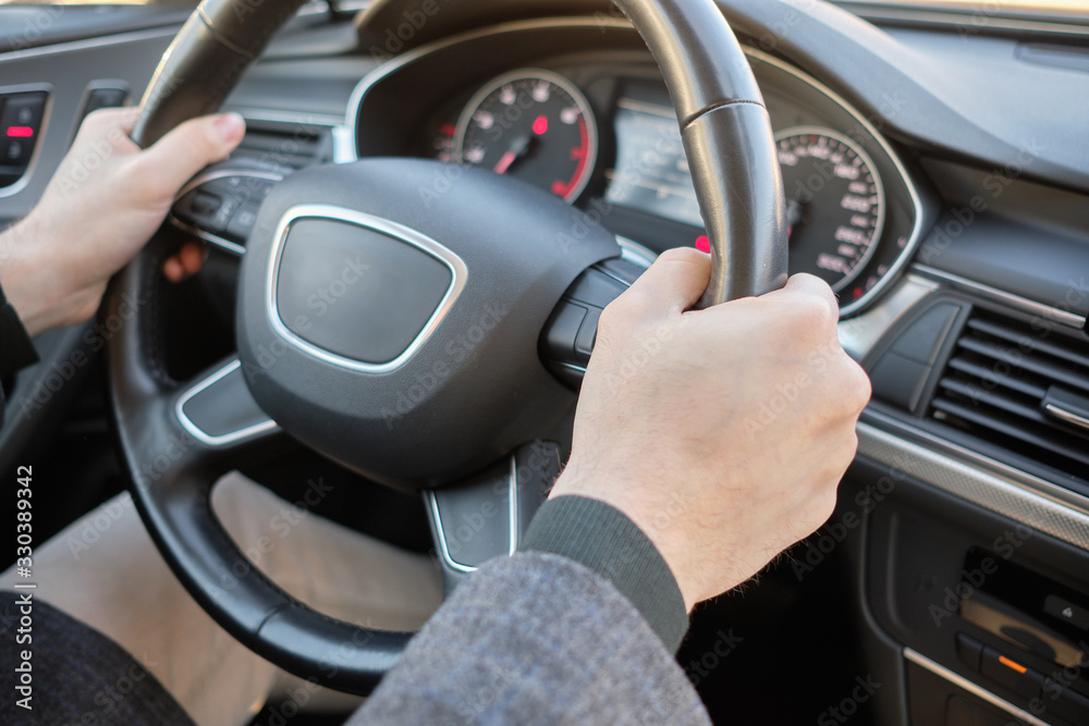 A man in a modern car. Hands holding the steering wheel in the correct location.