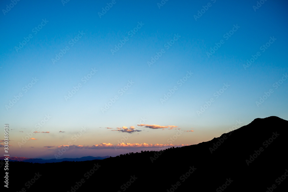 Mountain Silhouette againt Blue Sunset with Row of Pink Clouds
