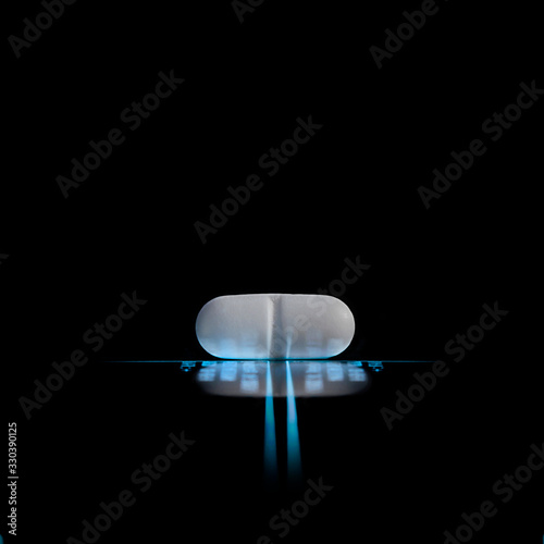 white pill on a luminous lines and blurred data on the black background with reflection
