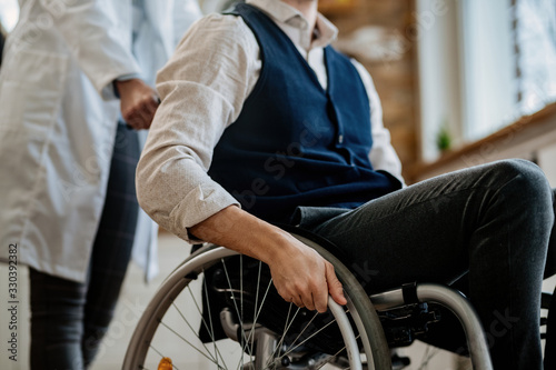 Unrecognizable nurse pushing wheelchair of male patient.