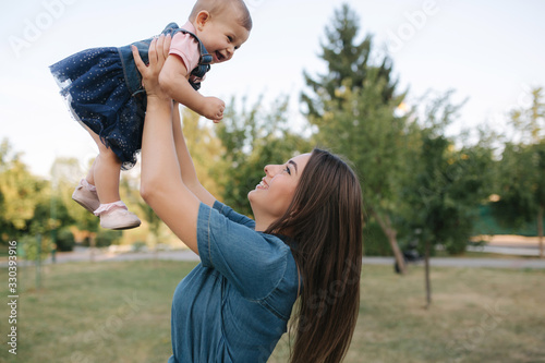 Cute baby on mom's hands outside. Family in the park in summer. Denim style. Mom and daughter in jeans