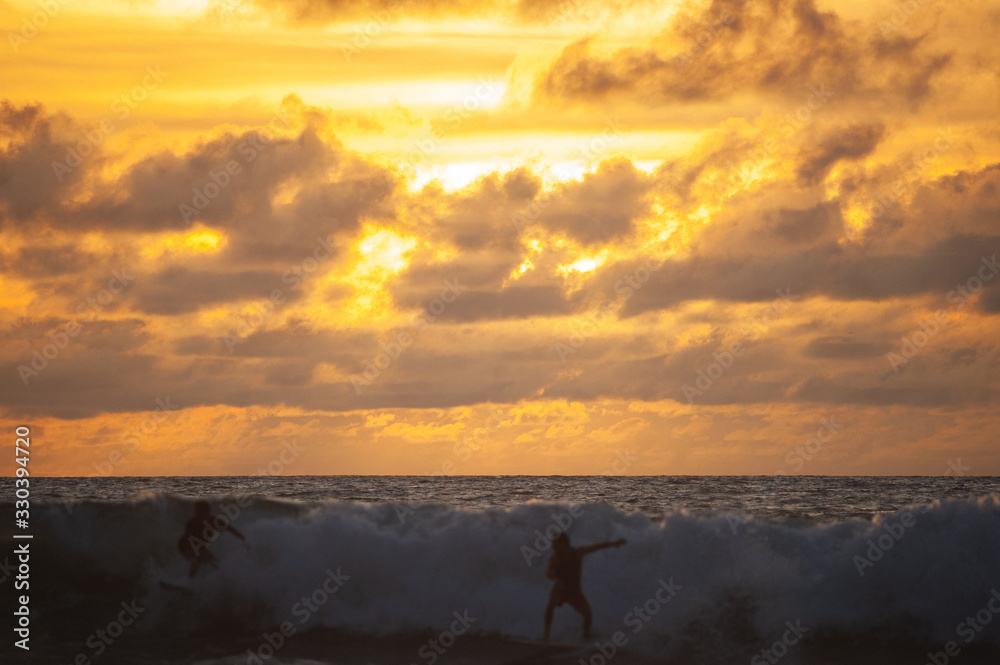 Young people ride on short boards, perform bright tricks on the waves during sunset.