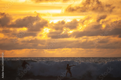 Young people ride on short boards, perform bright tricks on the waves during sunset.