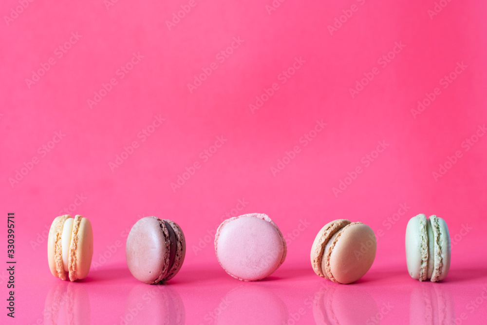 Close Up Fresh Colorful Macaroons In A Row Isolated On Pink Background, Sweet Colorful Biscuits Heap Lined Up With Reflection On Table Close Up Fresh Colorful Macaroons In A Row Isolated On Pink Background, Sweet Colorful Biscuits Heap Lined Up With Reflection On Table