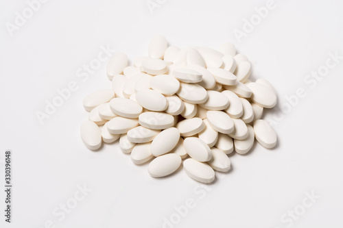 A pile of white oval-shaped tablets on a white background. View from the side