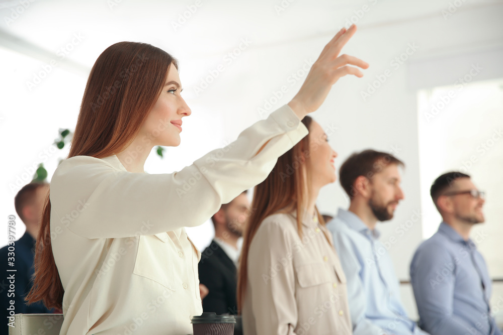 Fototapeta premium Young woman raising hand to ask question at business training indoors