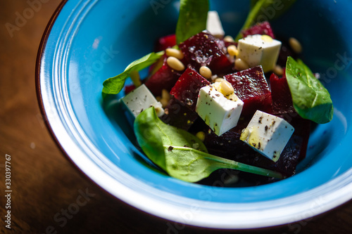 Salad with beetroot and feta cheese, spinach leaves, toasted pine nuts in blue ceramic bowl. For food blogs, restaurant menus, and content related to vegetarian or Mediterranean cuisine