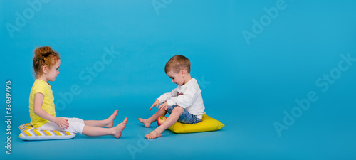 Positive cute toddler and redhead curly girl on the pillows are playing with apple on the blue background.Summer vacation and holidays concept,travel with children.Copy space.