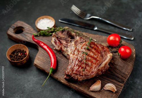 Grilled beef steak with spices and cutlery on a cutting board on a stone background with copy space for your text