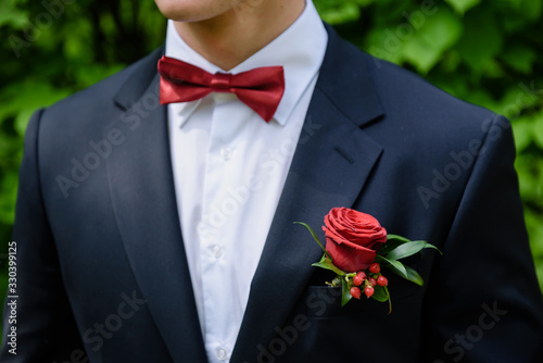 Close up portrait, man ties a bowtie at the collar, red bow on his white shirt. Groom