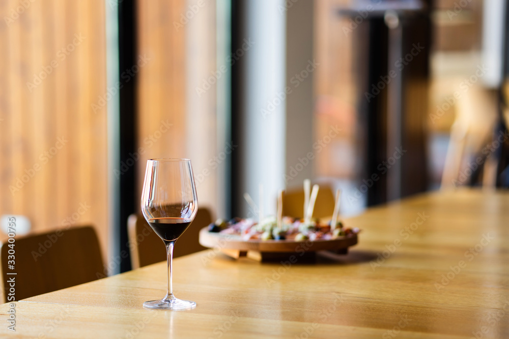 Glass of red wine on the table at home or restaurant in front of the defocused blur appetizer by the window Glass of red wine on the table at home or restaurant in front of the defocused blur appetizer by the window