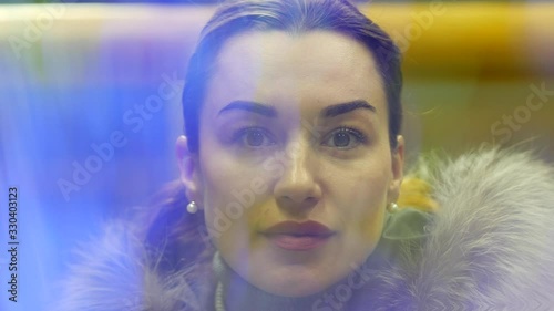 Young pretty lady perceptively looks at viewer via vibrating luminous fiber optic threads. Portrait of successful woman in jacket with fur collar through veil of blue light. Future technology concept photo