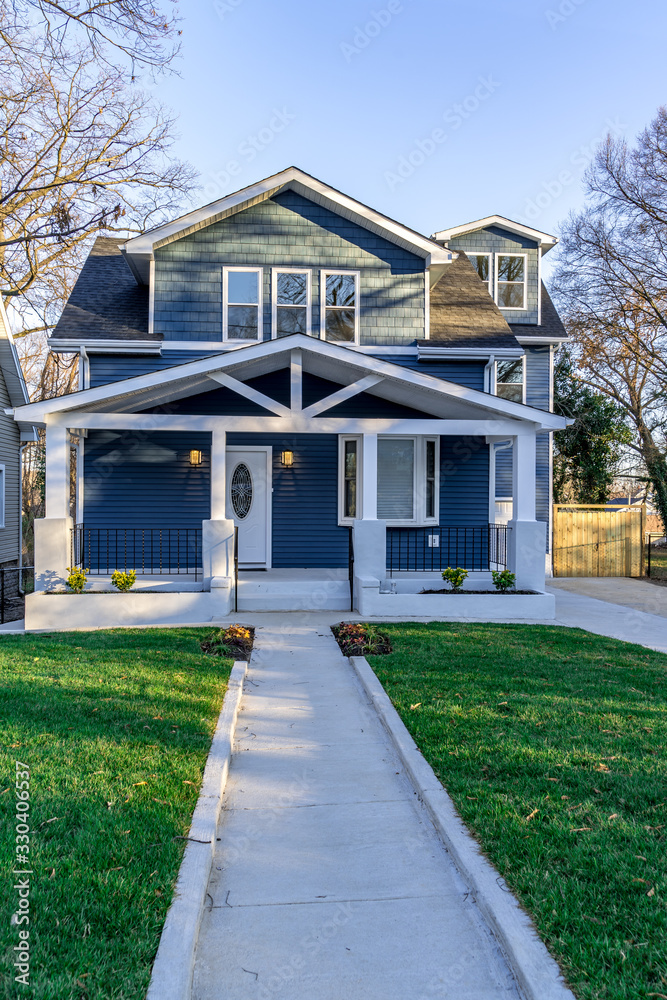 Newly restored craftsman style house with clean white lines adding accent to the blue horizontal vinyl siding, paved pathway leading to the covered porch in East Coast USA
