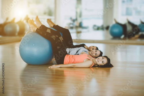 Three healthy Asian women are exercising with yoga-ball in the room. Woman in sportswear is performing yoga on a fitness-ball in the room. Concept for health care.