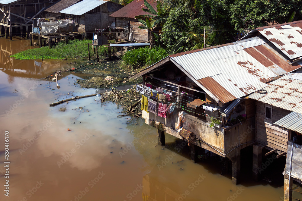 Old makeshift wooden houses on the banks of a dirty river - a slum of southeast asia