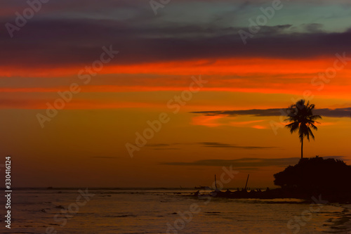 Dark silhouettes of palm trees and multicolored cloudy sky at sunset in the tropics on the beach. Copy space © alexey_arz