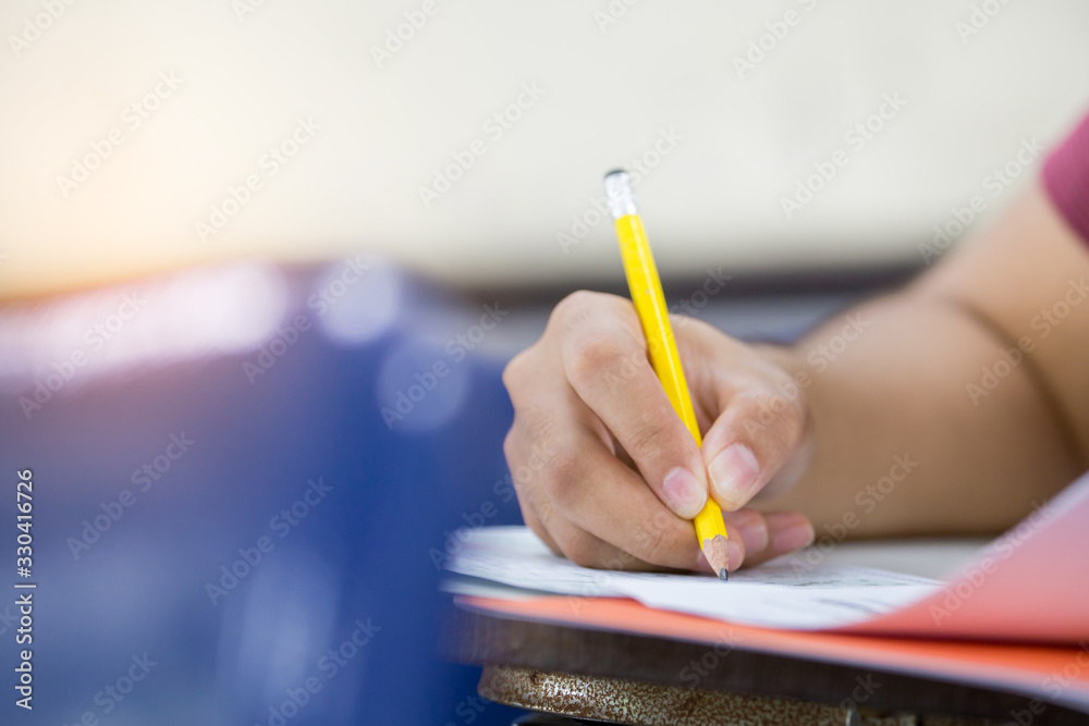 © panitan - high school,university student study.hands holding pencil writing paper answer sheet.sitting lecture chair taking final exam attending in examination classroom.concept scholarship for education abroad