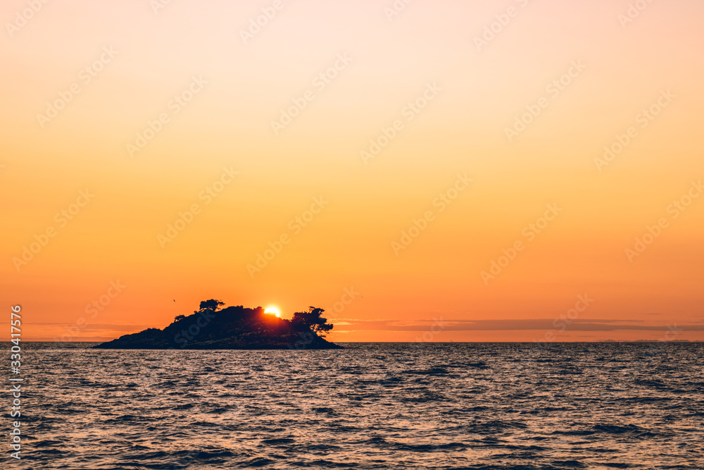 Romantic view of sunset over a deserted island in the distance at sea