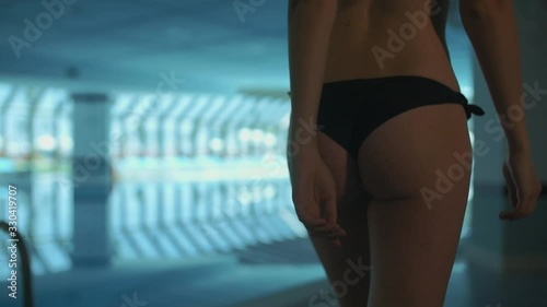 back view of young girl walking in bikini bottom by the pool covered with glass. Close-up image of her butt. in dim light. the back of it. sexy young girl.