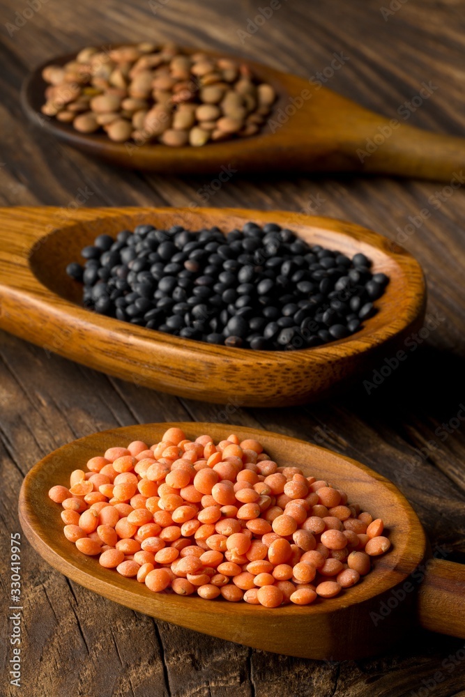 Different assorted lentils mix with red, brown and black beluga lentils in wooden scoops on brown wooden table background Different assorted lentils mix with red, brown and black beluga lentils in wooden scoops on brown wooden table background