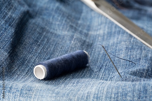 Blue yarn thread with needle and scissors on blue jeans denim close up - jeans fashion mending or repair concept
