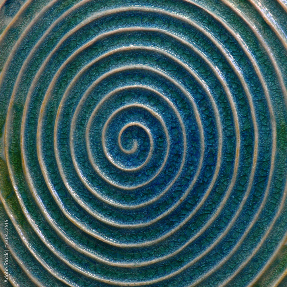 The ceramic image of a spiral with light rounds against the background of blue glaze. The ceramic image of a spiral with light rounds against the background of blue glaze.