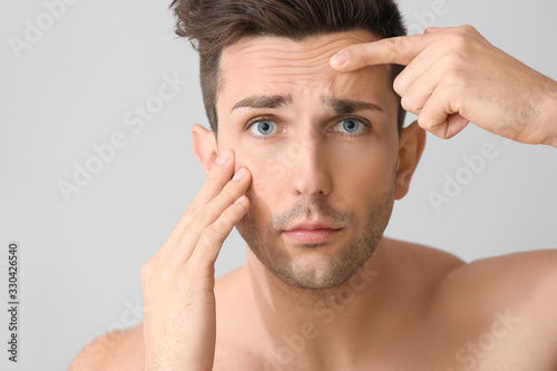 Young man worried about his appearance on light background. Plastic surgery concept