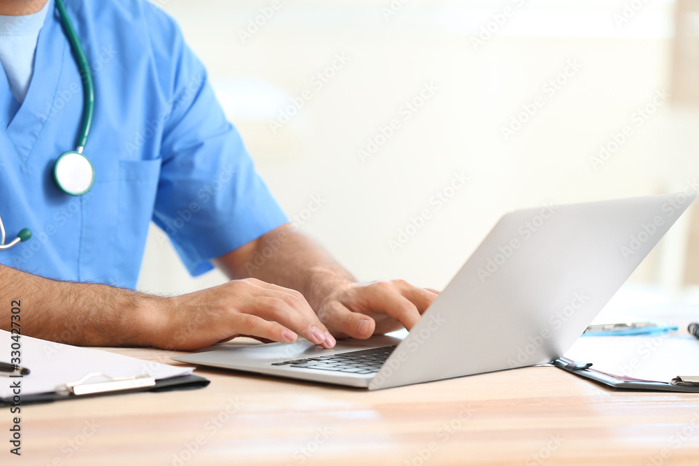 Young male doctor working on laptop in clinic, closeup Young male doctor working on laptop in clinic, closeup