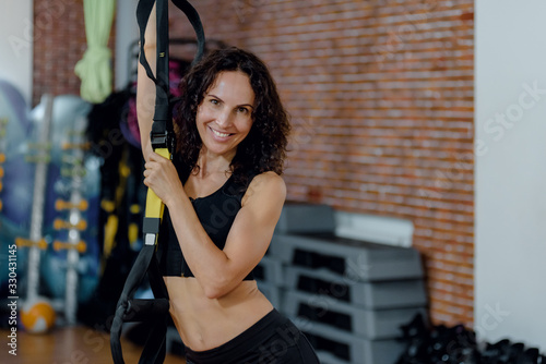 Portrait of smiling brunette woman training with suspension straps