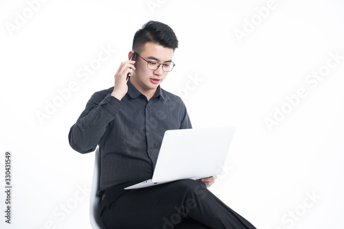 A young Asian man is using his mobile phone and laptop