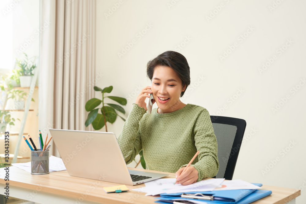 Woman working on laptop at home while talking on phone Woman working on laptop at home while talking on phone