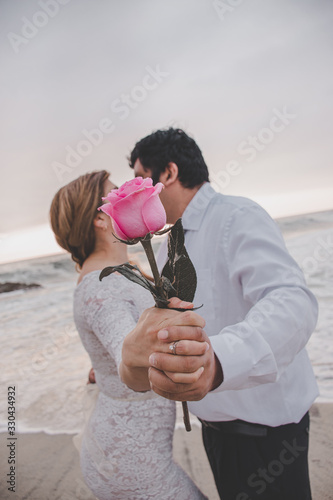 Pareja de novios con rosa  que  oculta el beso en la playa al atardecer  photo