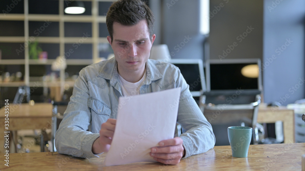 The Hardworking Young Designer Reading Documents in Modern Office The Hardworking Young Designer Reading Documents in Modern Office