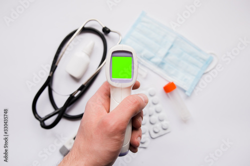 electronic thermometer in a man’s hand on the background of medicines