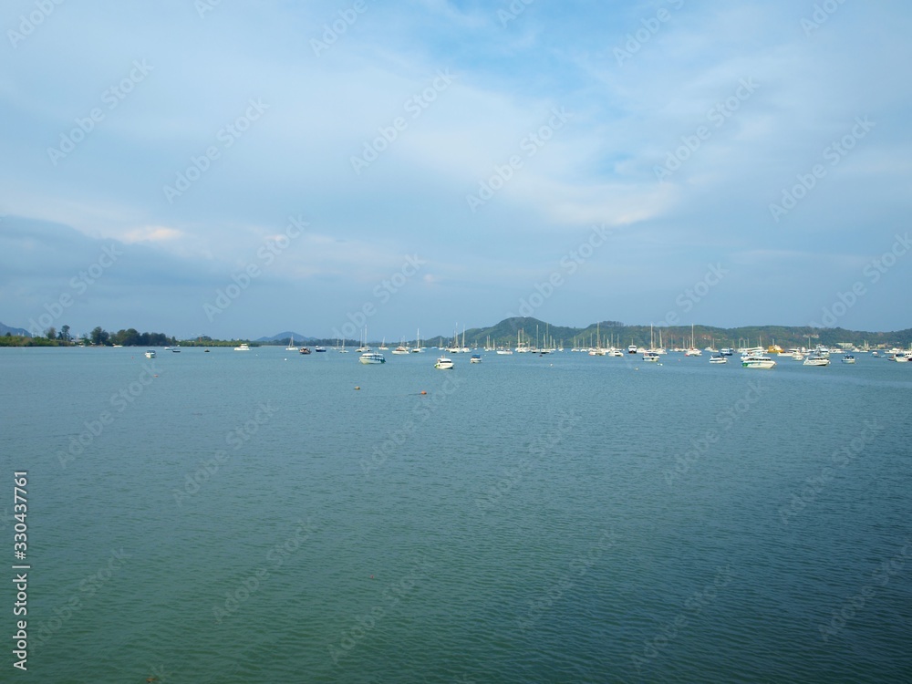 Seascape in the daytime. The view from the water to the shore. A land and green hills on the skyline. Boats and yachts away on the horizon. Landscape of cloudy sky and island. Panoramic view.