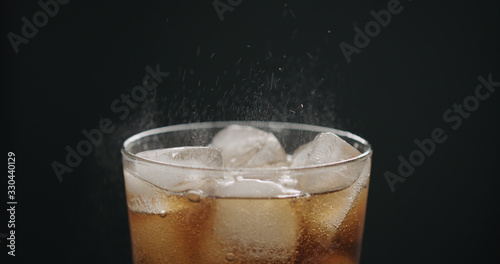 cola in glass with ice cubes on black background closeup